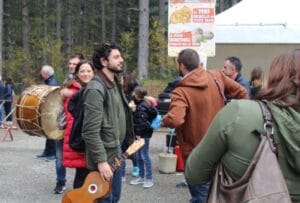 Persone partecipano alla sagra della salsiccia e della patata silana; due musicanti e altra gente in coda agli stand tipici della tradizione calabrese.